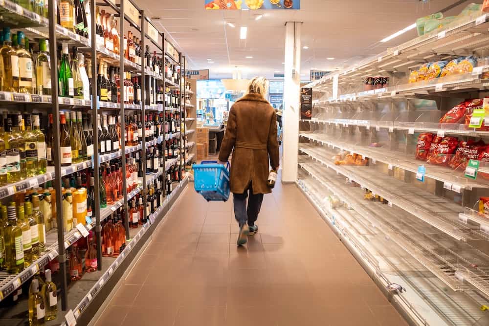 Woman in a supermarket aisle, with mostly empty shelves
